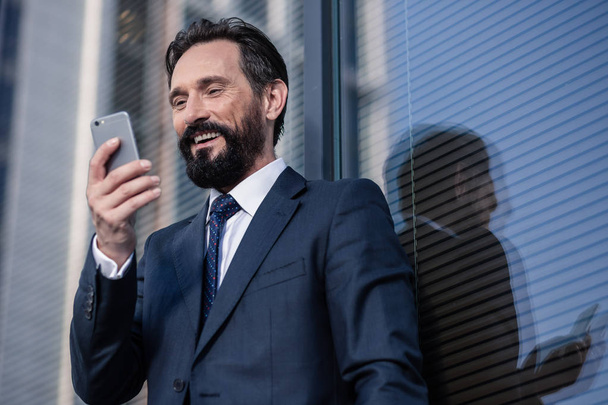 Keep me posted. Cheerful bearded businessman smiling while using his phone - Fotó, kép