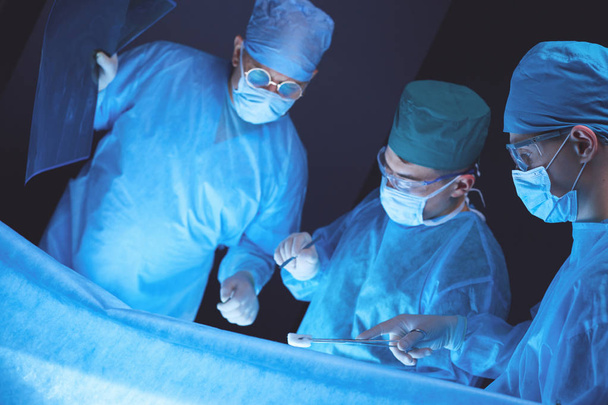 Group of surgeons at work in operating theater toned in blue. Medical team performing operation - Foto, imagen