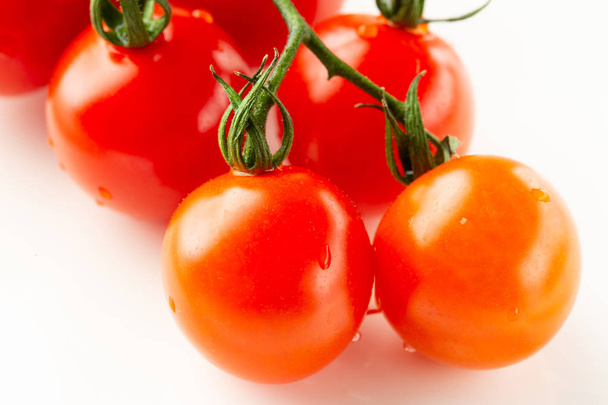 Close up photo of the branch of cherry tomatoes on white surface and two wet ripe tomatoes on the foreground - Fotoğraf, Görsel