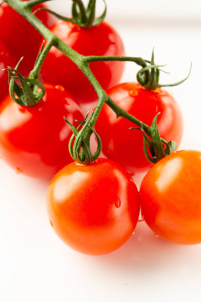 Close up photo of the ripe tasty red tomatoes on the green branch lying on the white surface and having water drops on them - Fotó, kép