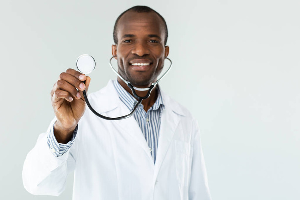 Ready to use. Cheerful afro american doctor using stethoscope while smiling - Фото, изображение