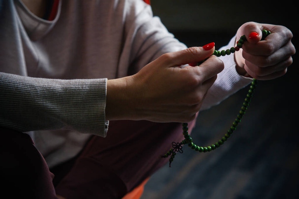 Close up of the woman in casual clothes holding green string of beads in her hands - Foto, Bild