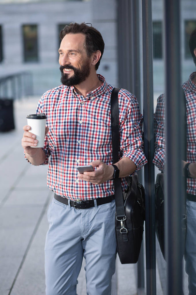 Coffee lover. Cheerful bearded man drinking coffee while standing near office building - Fotoğraf, Görsel