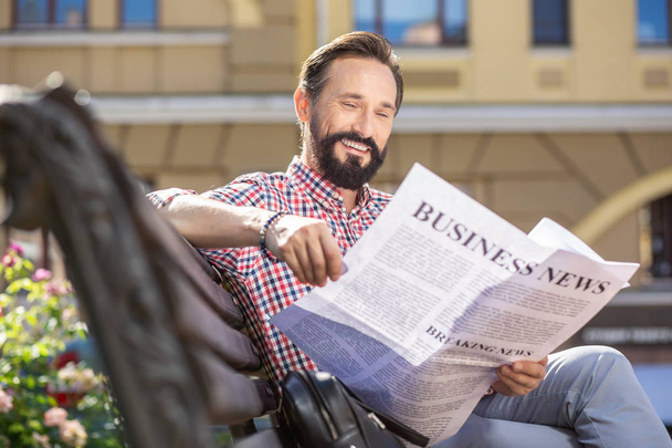 朝の習慣。ベンチに座りながら新聞を読む大人の男の心地よい笑顔 - 写真・画像