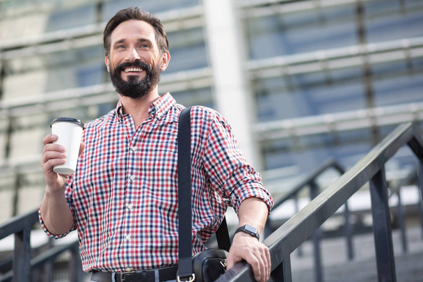 Open minded person. Cheerful bearded man walking in the city while drinking coffee - Foto, Bild