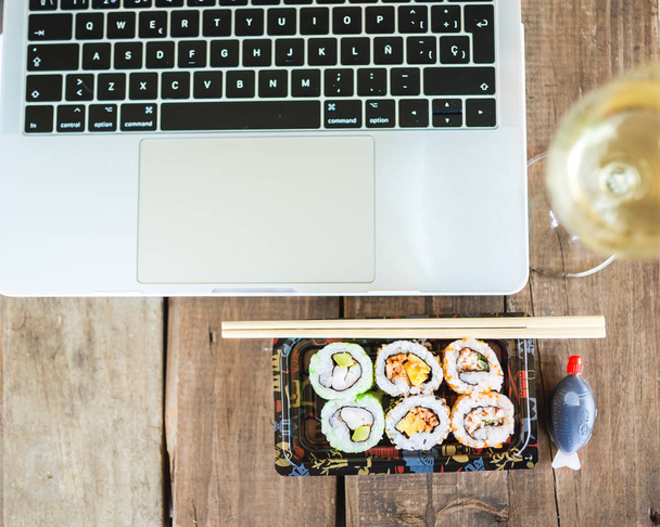 Tasty sushi rolls and laptop at wooden table. Food delivery. Workplace at home - Фото, зображення