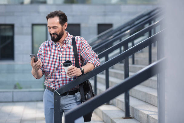 Live in the city. Smiling bearded man using phone while standing in urban settings - Foto, imagen