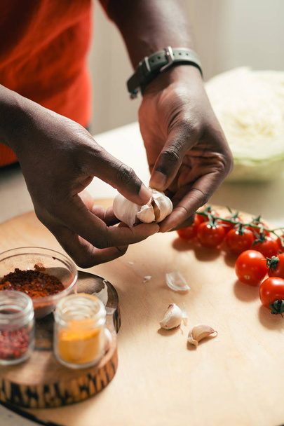 Cutting board with cherry tomatoes and spices on it and hands of man holding garlic above the board - Foto, imagen