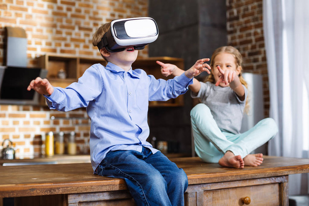 Real simulation. Positive little boy testign VR device while resting with his sister - Foto, imagen