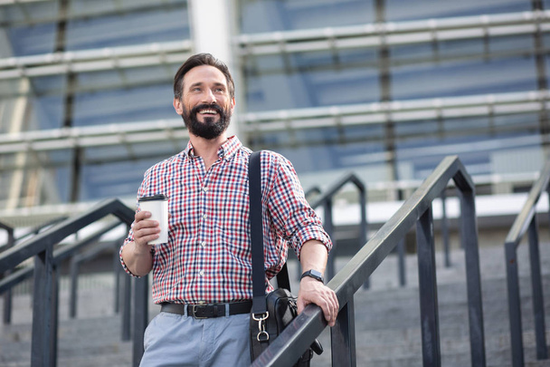 Nice start of the day. Cheerful smiling man drinking coffee while walking in urban settings - Foto, imagen
