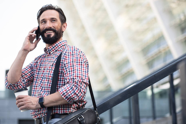 Glad to talk to you. Overjoyed pleasant man smiling while talking on phone outdoors - Valokuva, kuva