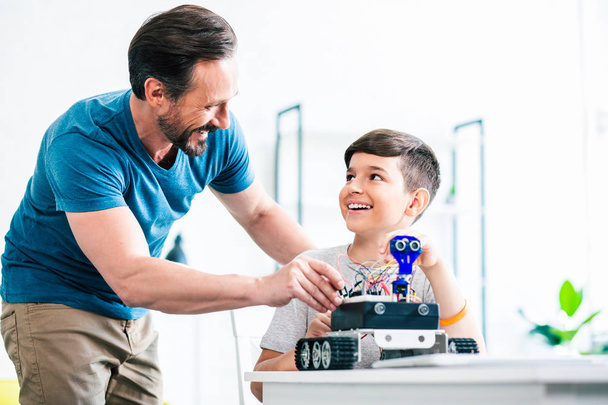 Cheerful handsome man helping his son while testing new robotic device at home - Foto, Bild