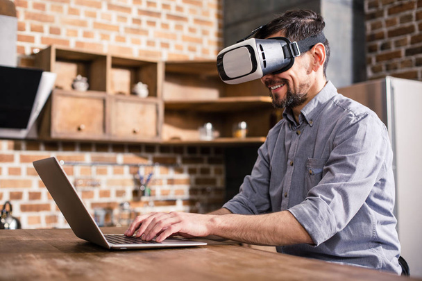 New start up. Joyful handsome man using his laptop while wearing VR device - Фото, изображение