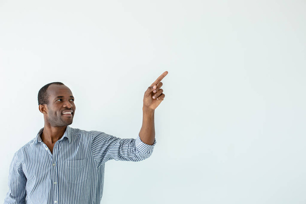 Νέες ικανότητες. Εύθυμος χαμογελαστός Αφροαμερικανός άνθρωπος που σημαδεύει στην άκρη ενώ στέκεται ενάντια στο λευκό φόντο - Φωτογραφία, εικόνα