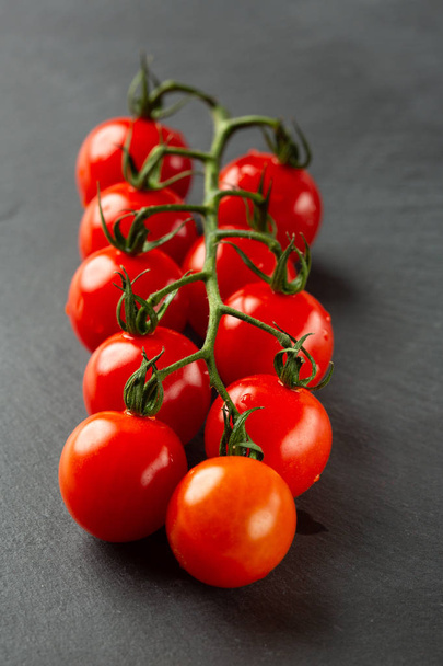 Close up photo of the black slate surface with a branch of fresh ripe tomatoes on it - Fotoğraf, Görsel