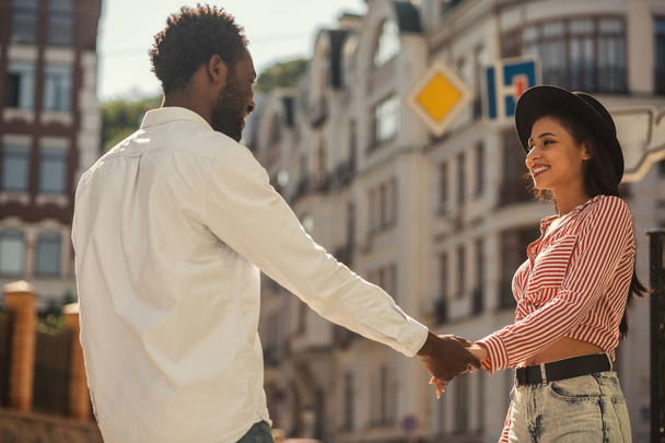 Young man and woman standing opposite each other and holding hands while smiling to each other in the street - Photo, Image