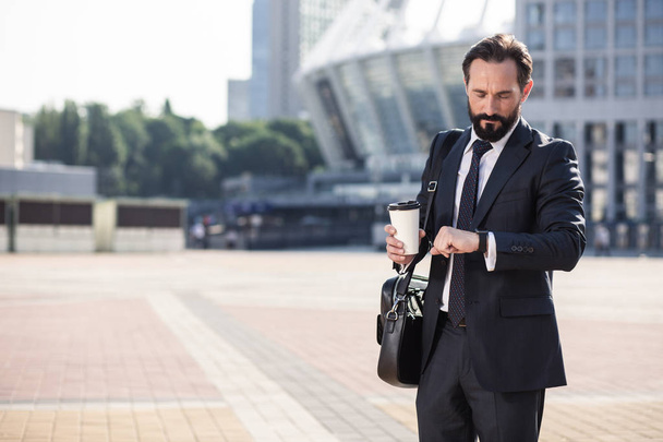 Modern way of life. Professional handsome businessman checking time while standing in the city - 写真・画像