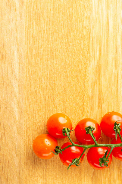 Top view of wooden table and cherry tomatoes branch lying on it and looking clean. Copy space at the top of the photo - Foto, Imagem