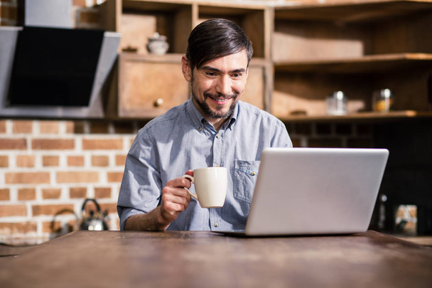 Pleasant morning. Cheerful man drinking coffee while reading news online - Photo, Image
