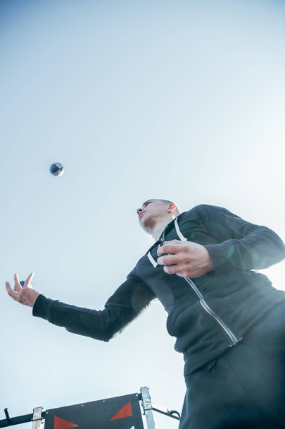 Concentrated young man in dark sports clothes standing outdoors and carefully throwing the balls into the air - Фото, зображення