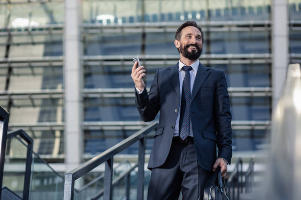 Anticipated call. Cheerful bearded businessman holding a phone while going to workplace - Valokuva, kuva