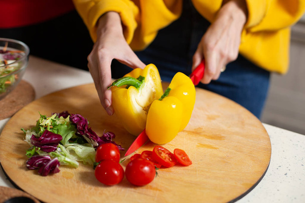Close up of hands of woman using red sharp knife while cutting yellow fresh paprika on the cutting board - Fotoğraf, Görsel