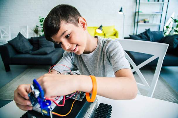 Positive smart schoolboy experimenting with his robotic device while working on his engineering project - Foto, Bild