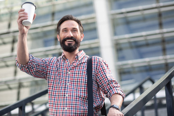 Glad to see you. Positive adult man drinking coffee while welcoming a passer by outdoors - 写真・画像