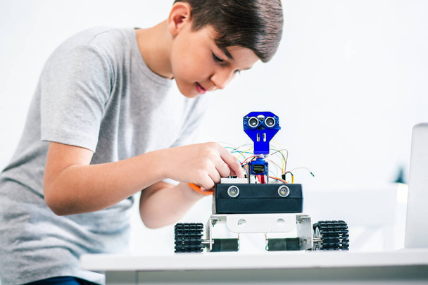 Concentrated smart little boy constructing a robot while improving his engineering skills - Foto, afbeelding