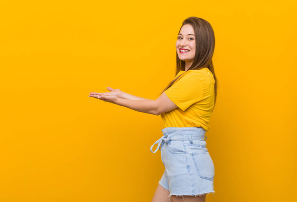 Young woman teenager wearing a yellow shirt holding a copy space on a palm. - 写真・画像