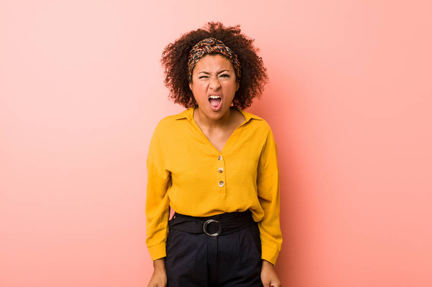 junge afrikanisch-amerikanische Frau vor rosa Hintergrund schreit sehr wütend und aggressiv. - Foto, Bild
