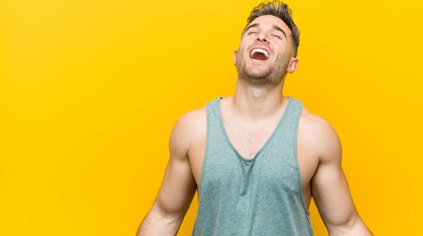 Mladý fitness muž proti žluté pozadí se uvolnil a šťastně se smál, krk se roztáhl na zuby. - Fotografie, Obrázek