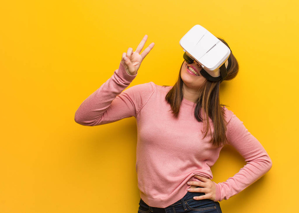 Young cute woman wearing a virtual reality googles showing number two - Photo, Image