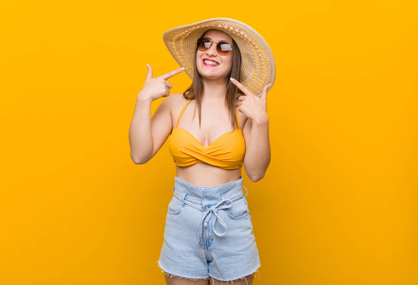 Young caucasian woman wearing a straw hat, summer look smiles, pointing fingers at mouth. - Foto, imagen