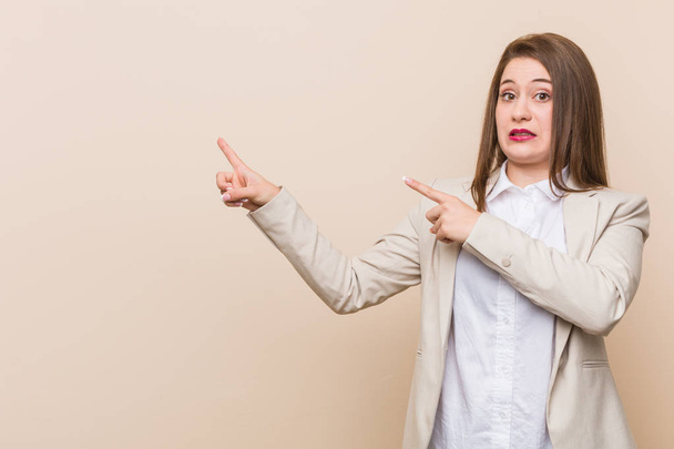 Young business woman shocked pointing with index fingers to a copy space. - 写真・画像