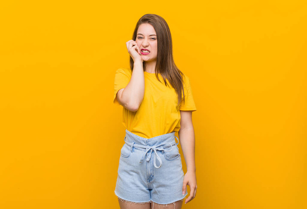 Молодая женщина-подросток в жёлтой рубашке грызет ногти, нервничает и очень беспокоится.
. - Фото, изображение