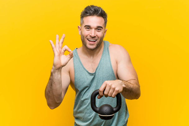 Caucasian man holding a bumbbell cheerful and confident showing ok gesture. - Foto, immagini