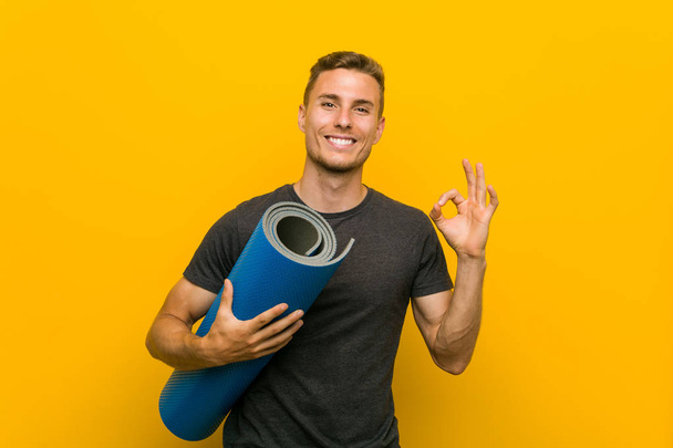 Young caucasian man holding a mat cheerful and confident showing ok gesture. - Photo, Image