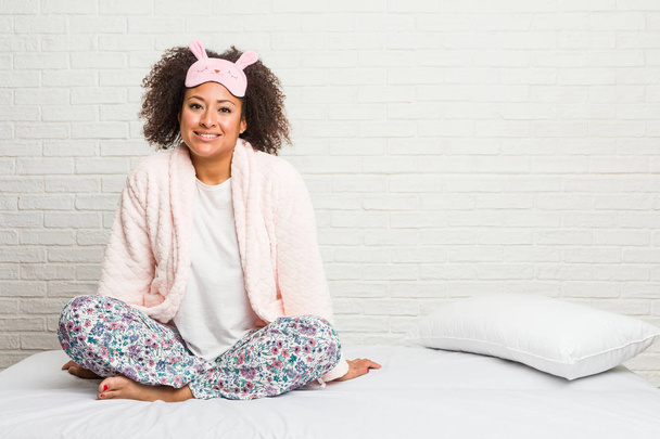 Νεαρή αφρικανική Αμερικανίδα στο κρεβάτι φορώντας πιτζάμες με αυτοπεποίθηση κρατώντας τα χέρια στους γοφούς. - Φωτογραφία, εικόνα