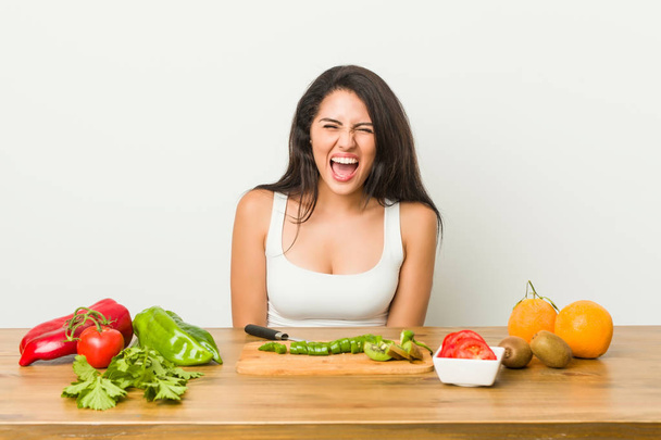 Mujer joven con curvas preparando una comida saludable gritando muy enojado y agresivo
. - Foto, Imagen