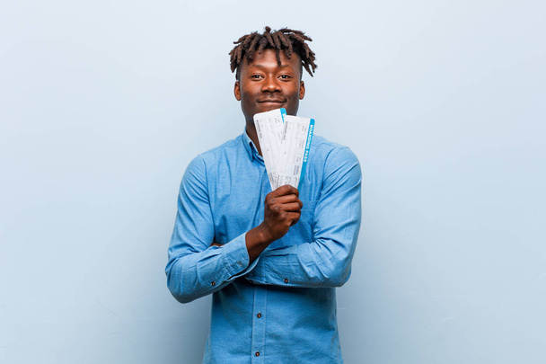 Young rasta black man holding an air tickets smiling confident with crossed arms. - Photo, Image