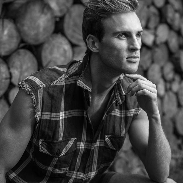 Young handsome man in casual shirt poses near wooden background. Black-white photo. - Fotó, kép