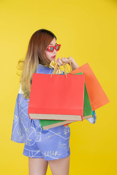 The girl holds a fashion shopping bag and holds a smart card on a yellow background. - Photo, Image