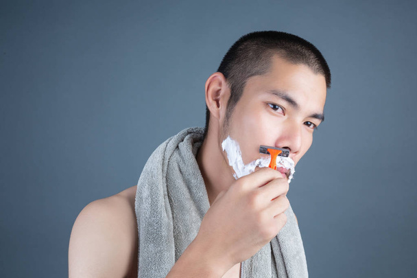 Shaving handsome guy shaved on the face on a gray background. - 写真・画像
