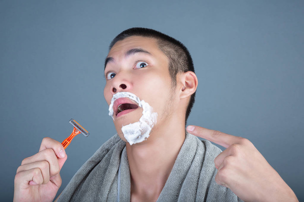 Shaving handsome guy shaved on the face on a gray background. - Φωτογραφία, εικόνα