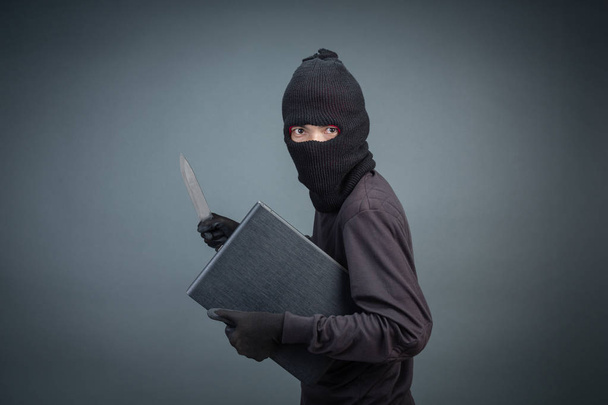 Male thieves steal a laptop computer on a gray background. - Foto, afbeelding