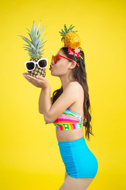 Beautiful woman in a swimsuit holding a pineapple poses on a yellow background. - Foto, afbeelding