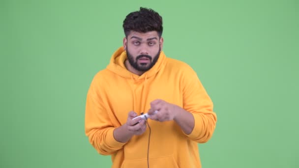 Tired young overweight bearded Indian man playing games and falling asleep - Záběry, video
