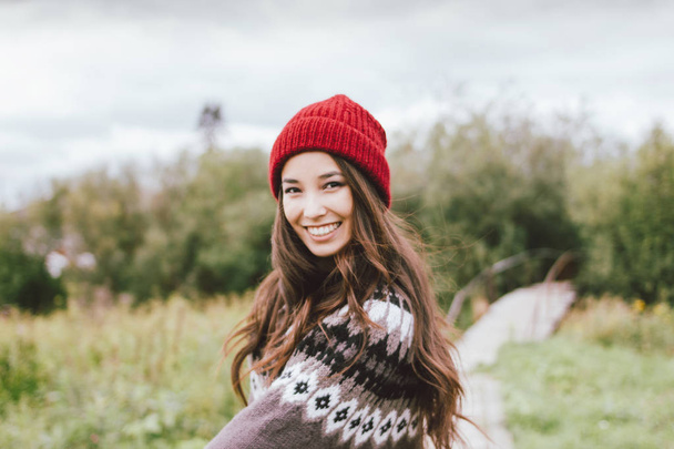秋の自然公園で赤い帽子とニットノルディックセーターで美しい気楽な長い髪のアジアの女の子 - 写真・画像