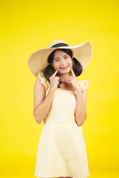 A beautiful, cheerful young woman with a big hat on a yellow background. - Photo, Image